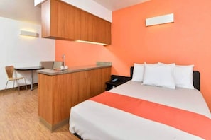 A hotel room with a bed, a desk, and a small kitchenette.