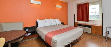 A hotel room with a bed, a desk, a chair, a window with curtains, and a wall-mounted heater.
