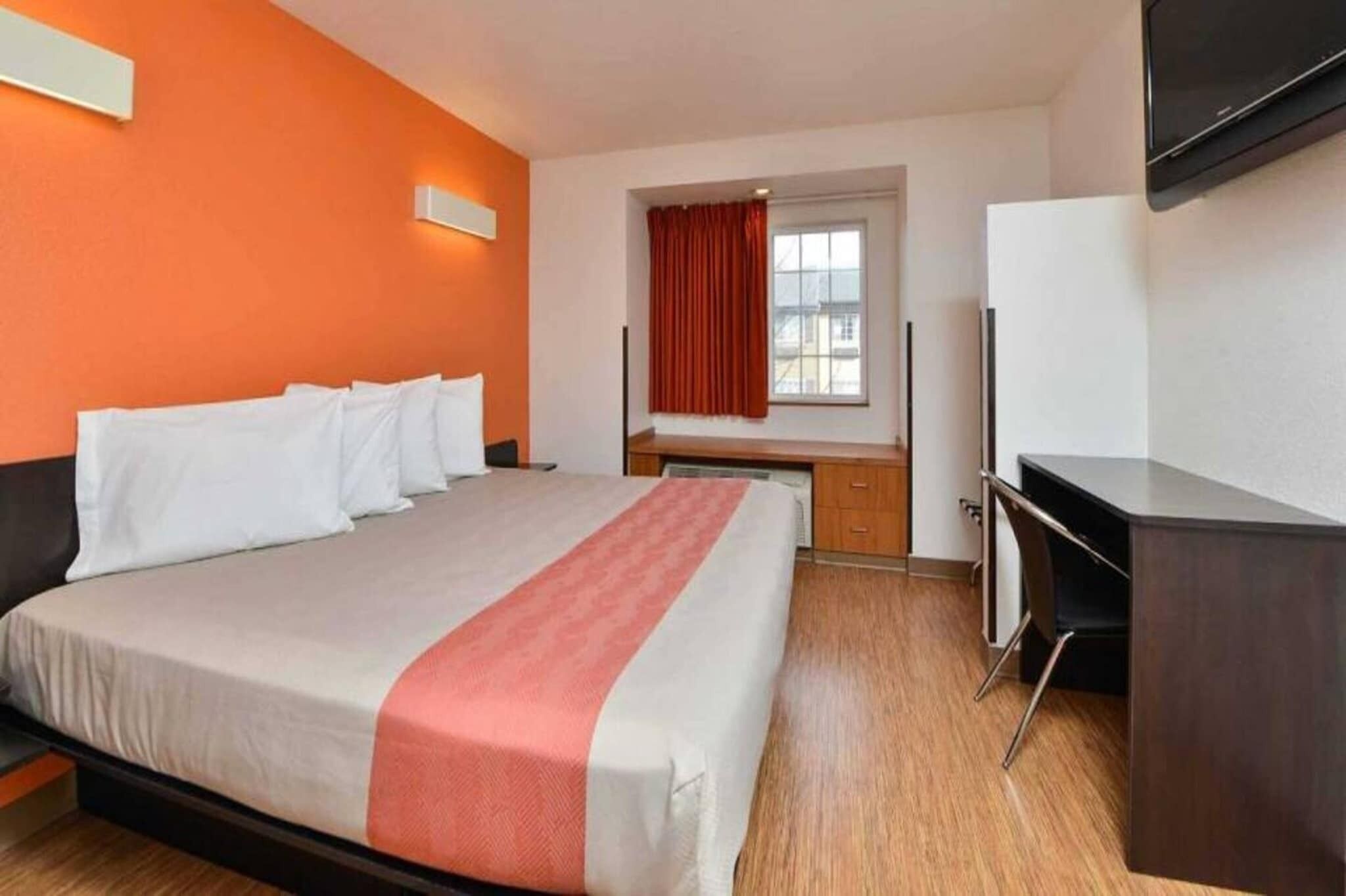 Habitación de hotel con cama, escritorio, silla, televisión y ventana con cortinas.