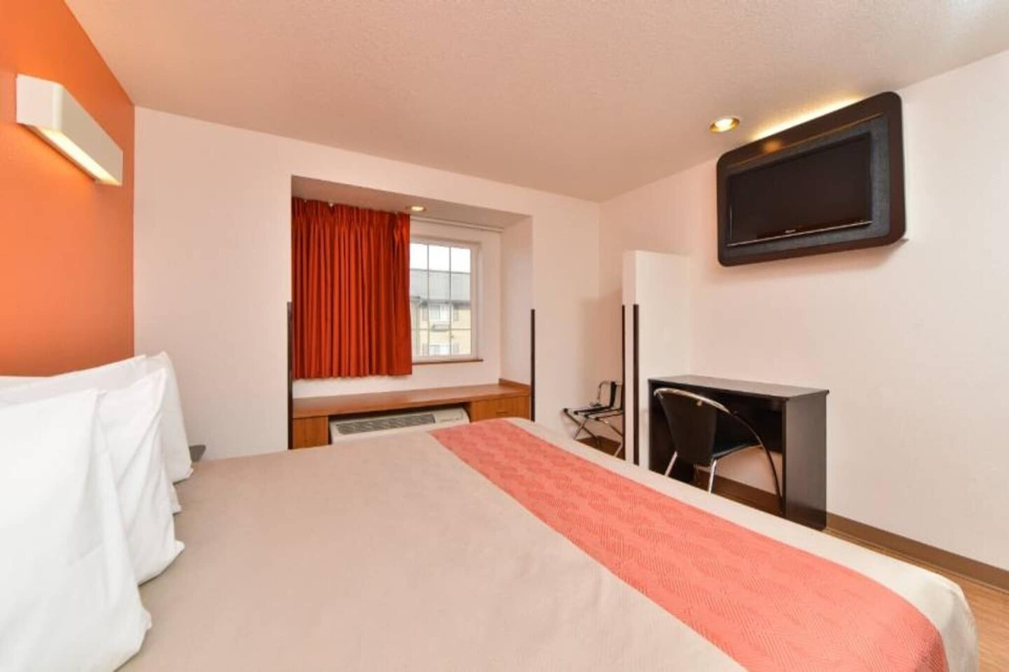 A hotel room with a bed, a desk, a chair, a television, and a window with curtains.