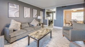 A living room with a grey sofa, a coffee table, and a grey armchair. There are abstract wall art pieces and a ceiling light. - Poolside Fun! Waterfront Gem Near San Marco Square (Jacksonville)
