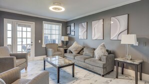 A living room with a grey sofa, a coffee table, and a lamp. There are abstract wall art pieces and a door with a view. - Poolside Fun! Waterfront Gem Near San Marco Square (Jacksonville)