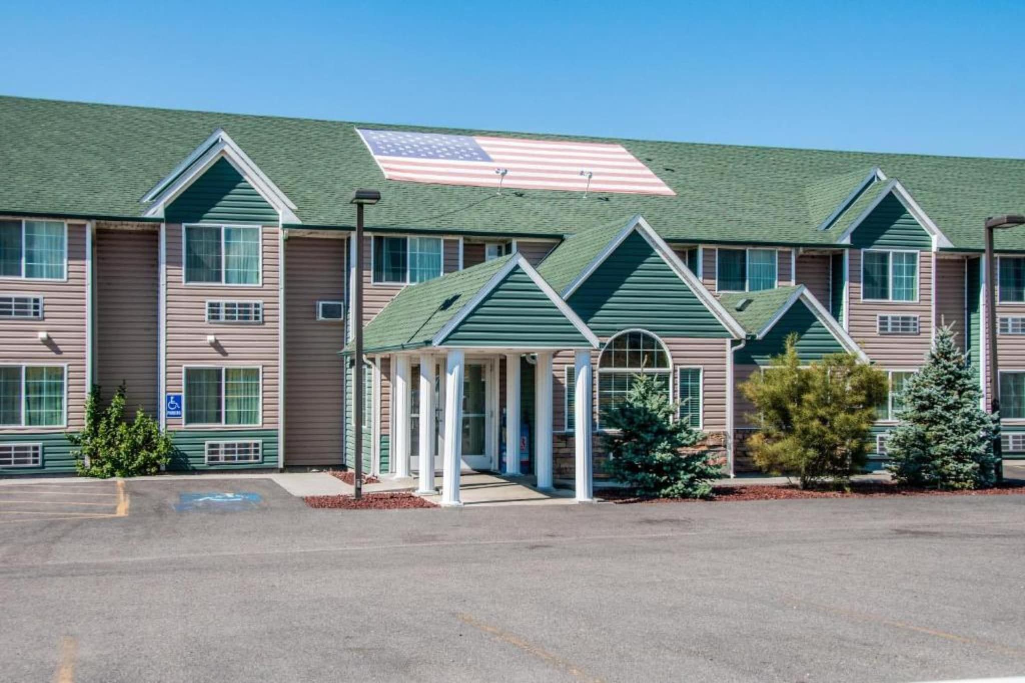 A multi-story hotel with a green roof, a covered entrance, and a parking lot.