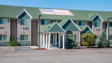 A multi-story hotel with a green roof, a covered entrance, and a parking lot.