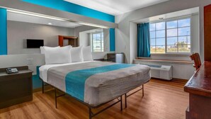 A modern hotel room with a large bed, a desk, a flat-screen TV, a window with curtains, and a view of the outdoors. - 1 Queen Bed | Suite, Nsmk, Micfridge, Sofa-Bed (Idaho Falls)