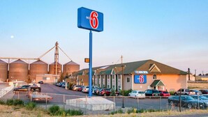 A motel with a large sign, a parking lot, and industrial buildings in the background. - 1 Queen Bed | Suite, Nsmk, Micfridge, Sofa-Bed (Idaho Falls)