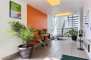 A hotel lobby with potted plants, a staircase, and a sign advertising a dough-saving app.