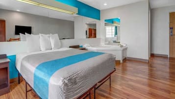 A modern hotel room with a large bed, a bathroom with a mirror, and a wooden floor.