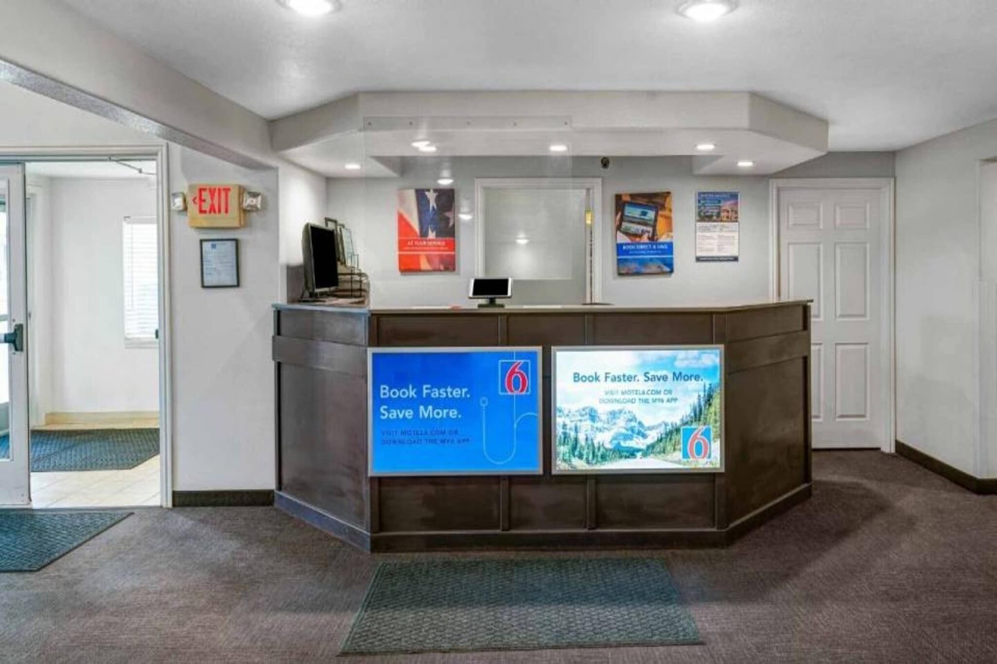A reception desk with a computer monitor, a sign for the exit, and two promotional posters.