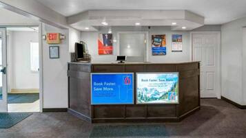 A reception desk with a computer monitor, a sign for the exit, and two promotional posters.