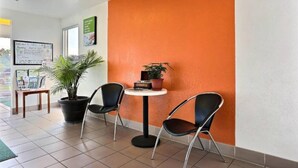 Ein Empfangsbereich mit Blumentopf, zwei Stühlen, einem kleinen Tisch und einer Kreidetafel mit Schrift.