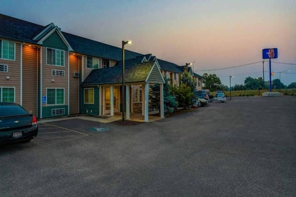 A motel with a parking lot, a small building with a porch, and a sign indicating the number 6.