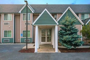 A two-story building with a green roof, a covered entrance, and a wheelchair-accessible sign.