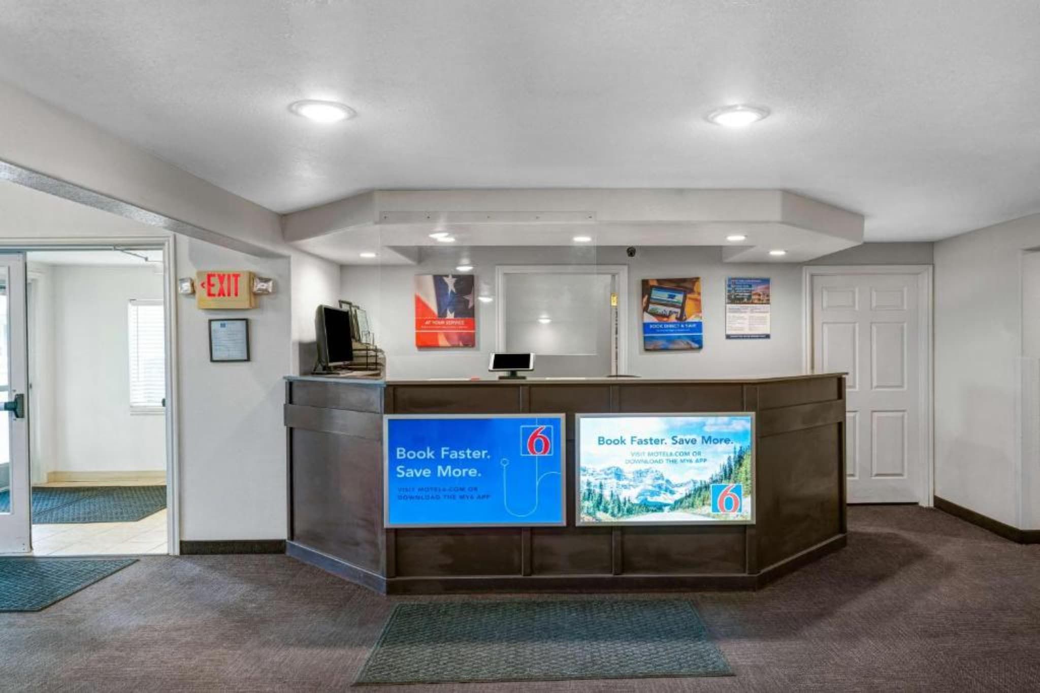A reception desk with a digital screen displaying a booking message, a sign for a 6-star rating, and a wall-mounted sign promoting a mobile app.