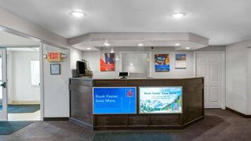 A reception desk with a digital screen displaying a booking message, a sign for a 6-star rating, and a wall-mounted sign promoting a mobile app.