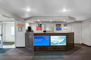 A reception desk with a digital screen displaying a booking message, a sign for a 6-star rating, and a wall-mounted sign promoting a mobile app.