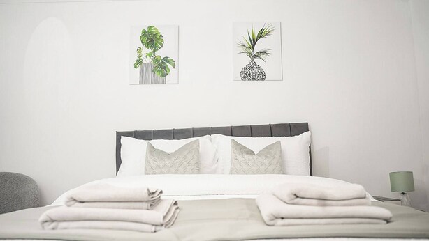 A neatly made bed with pillows and a folded blanket, a bedside lamp, and two framed plant illustrations on the wall. - Sleeps 4, Great for Groups, Free Parking Kent (Medway)