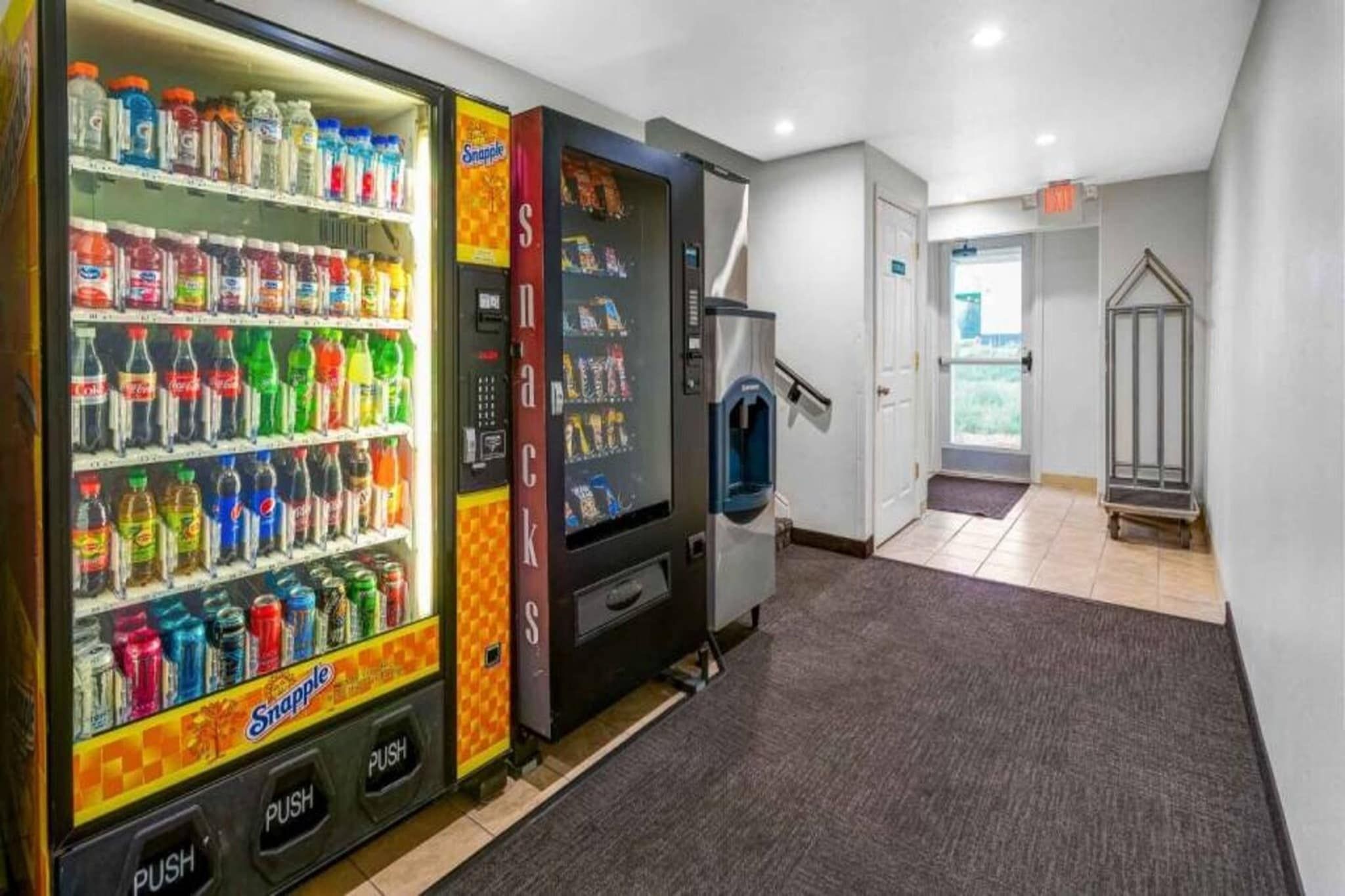 Een automaatgedeelte met diverse dranken en snacks, een trap en een deur naar een andere ruimte.