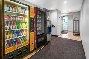 Een automaatgedeelte met diverse dranken en snacks, een trap en een deur naar een andere ruimte.