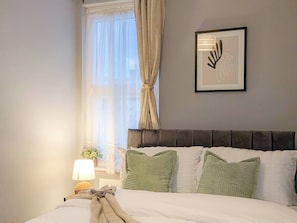 Une chambre d’hôtel avec un lit, une table de chevet, une lampe, un tableau encadré et une fenêtre avec des rideaux.
