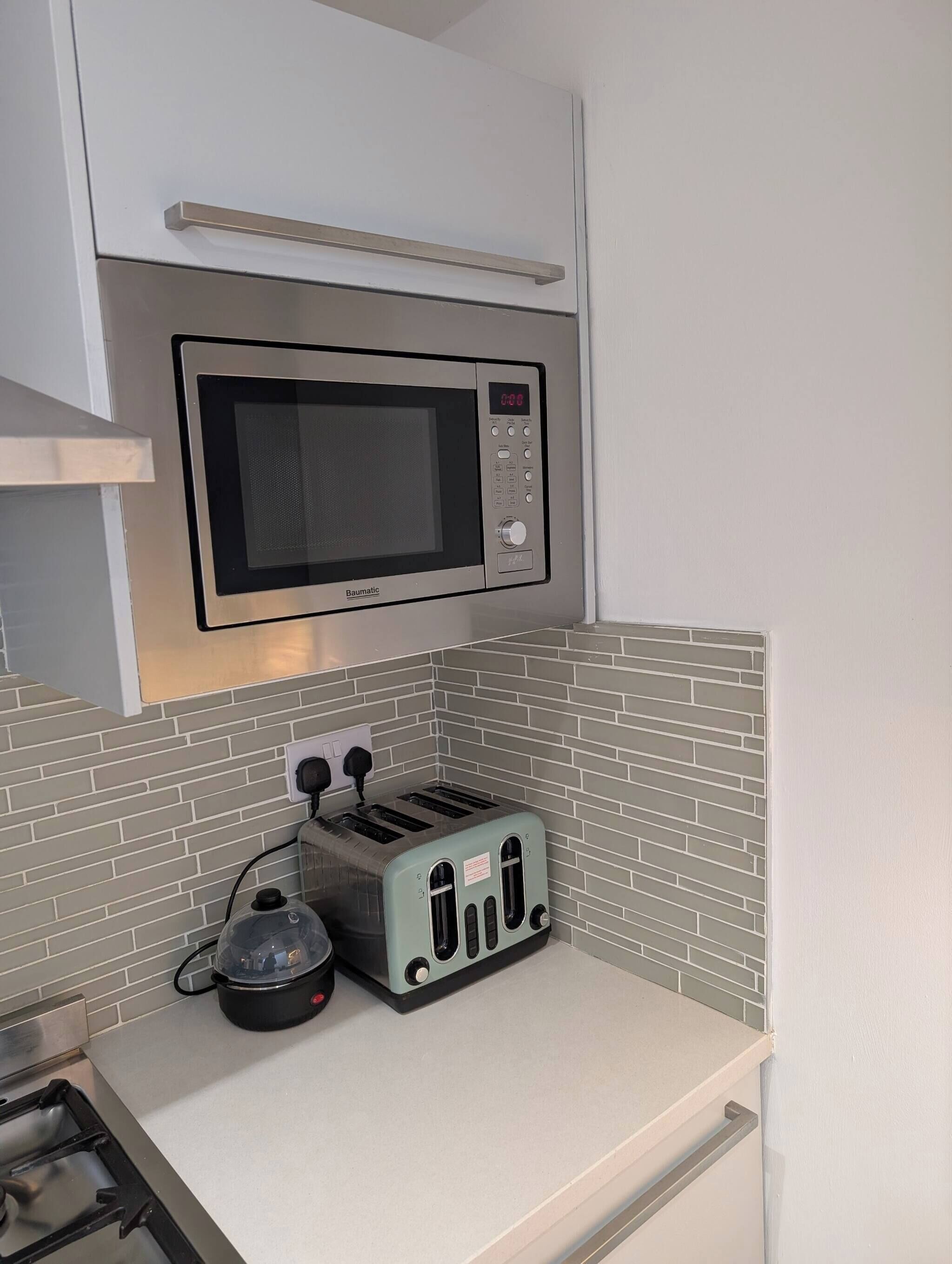 Une cuisine équipée d’un four à micro-ondes, d’un grille-pain et d’une bouilloire, le tout posé sur un plan de travail blanc.
