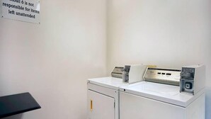 A laundry area with a washing machine and dryer, a small table, and a sign indicating the hotel is not responsible for unattended items.