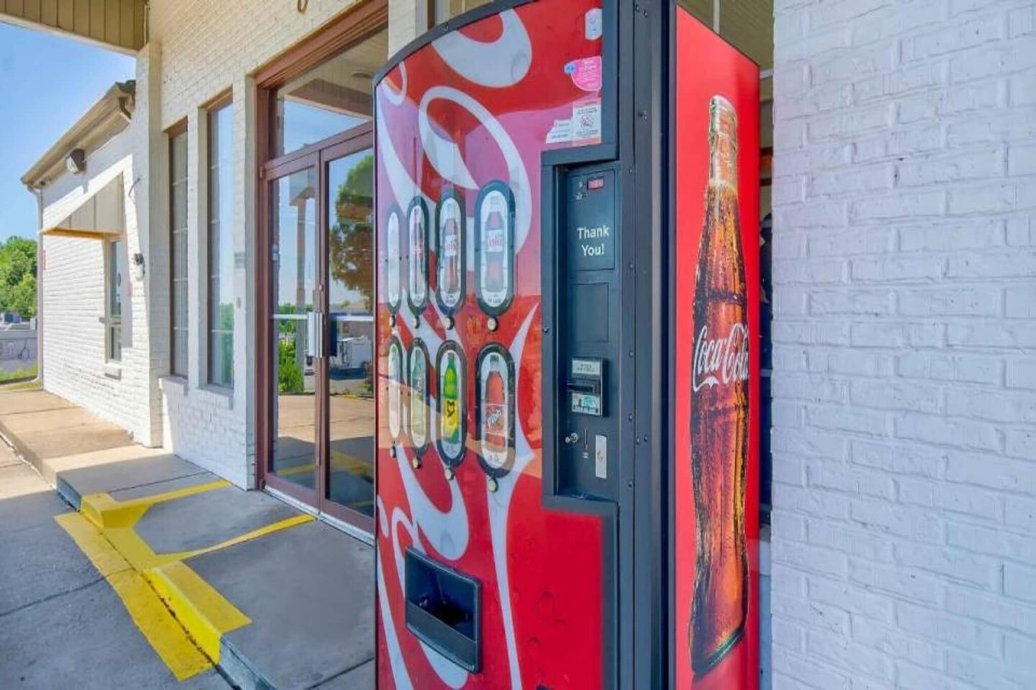Una máquina expendedora de Coca-Cola frente a un edificio con puertas de vidrio.