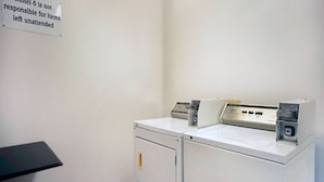 A laundry room with a washing machine and dryer, a sign indicating responsibility for unattended items, and a black table.