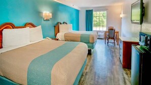 A hotel room with two beds, a desk, a chair, a TV, and a window.