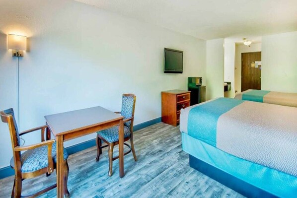 A room with a bed, a desk with a chair, a television, and a wall-mounted light fixture.
