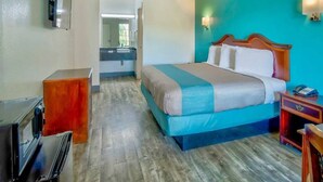 A hotel room with a bed, a desk, a mirror, and a television.