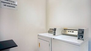 A laundry room with a washing machine and dryer, a sign indicating responsibility for unattended items, and a black table.