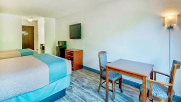A hotel room with a bed, a desk, a chair, a television, and a wall-mounted light fixture.
