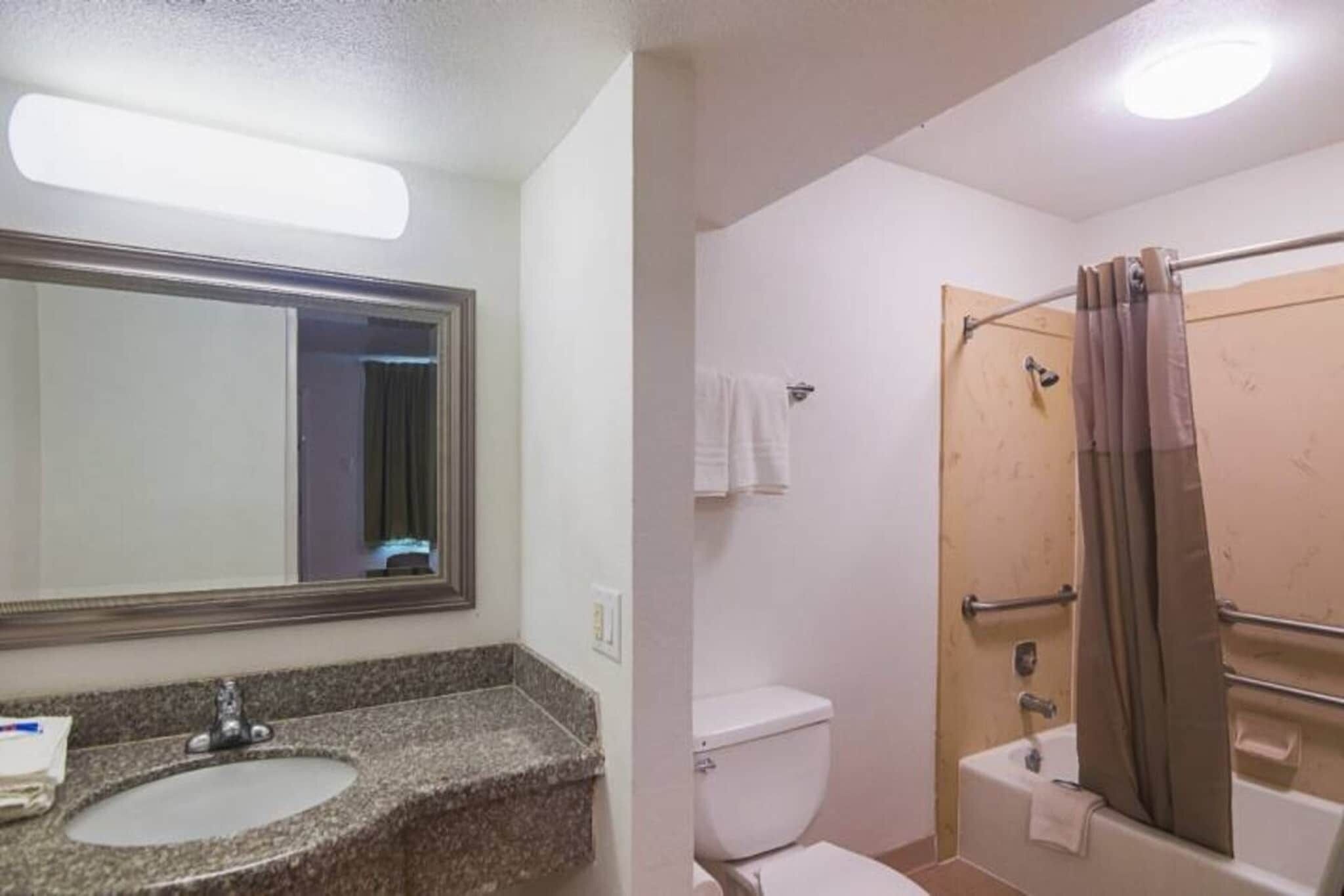 Une salle de bain avec un lavabo sur un plan de travail en granit, des toilettes blanches, une douche avec une porte en verre et un porte-serviettes.
