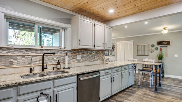 Una cocina con encimera de granito, pileta de acero inoxidable y muebles blancos.