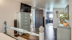 Un dormitorio con cama, cómoda, televisor y puerta que da a otra habitación.