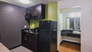 A compact kitchen with a microwave, stove, and refrigerator, a small sink, and a green accent wall. - 1 King Bed | Smoking, Kitchen (Tyler TX)