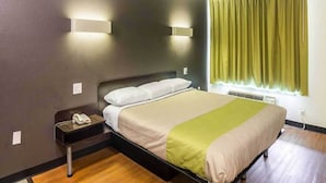 A single bed with a headboard, a bedside table with a phone, a window with curtains, and a wall-mounted light fixture. - 1 King Bed | Smoking, Kitchen (Tyler TX)