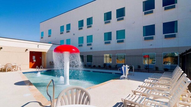Una piscina con fuente, sillas de descanso y un edificio con múltiples ventanales.