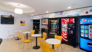 Un restaurante con sillas amarillas, mesas, un refrigerador de Coca-Cola, una máquina expendedora de Pepsi y un televisor en la pared.