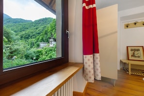 Una ventana con vista a una ladera boscosa, un banco de madera y un cuadro en la pared.
