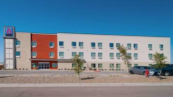 Un hotel moderno con fachada roja y blanca, múltiples ventanas y un estacionamiento.