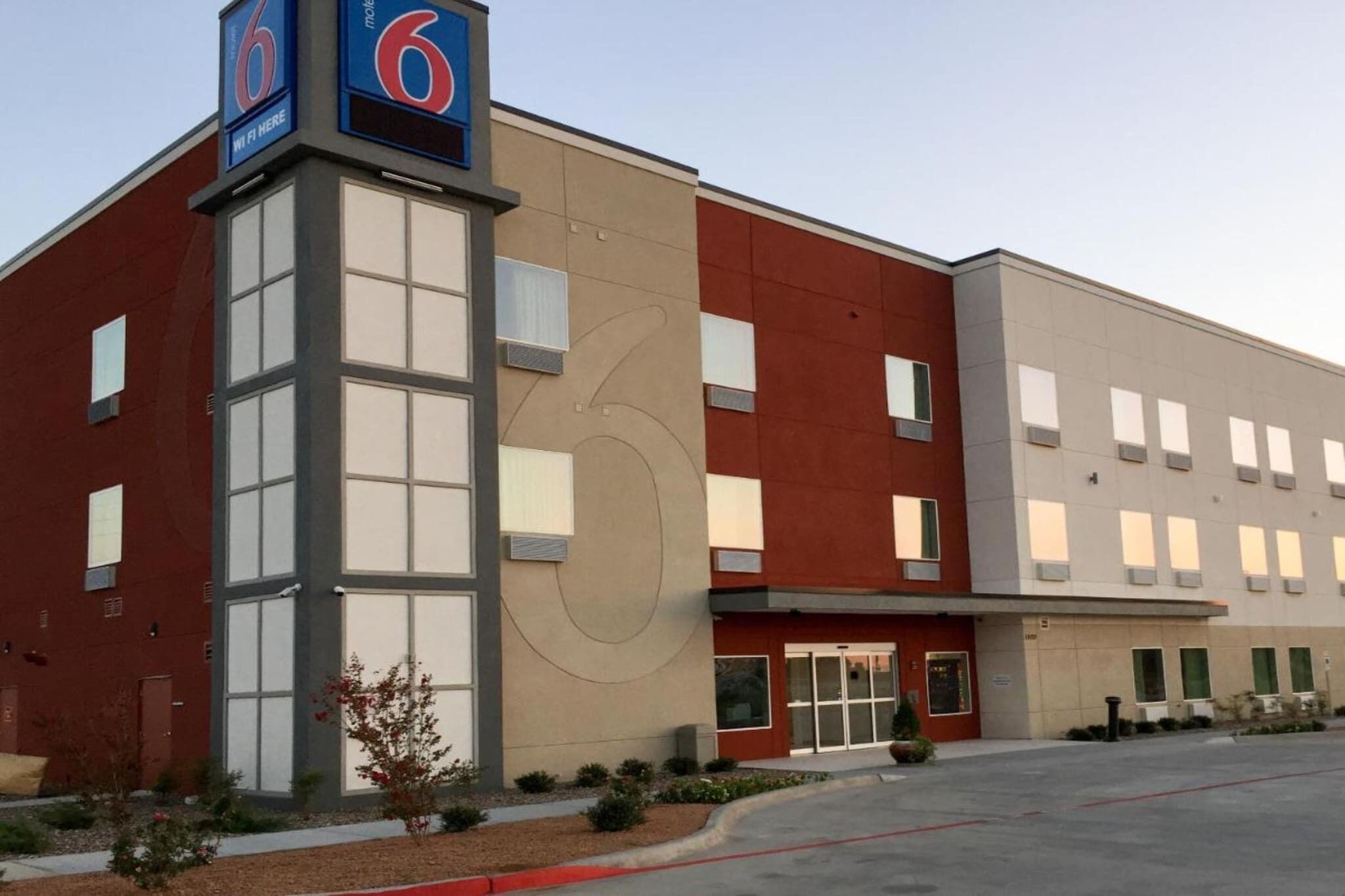 A modern building with a prominent '6' sign, large windows, and a parking lot.