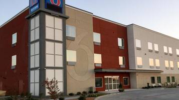 A modern building with a prominent '6' sign, large windows, and a parking lot.