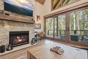 Ein Steinkamin mit Fernseher darüber, ein Holztisch mit Büchern und ein Balkon mit Sitzgelegenheit.