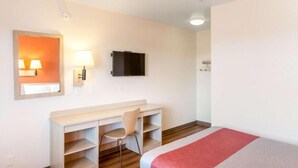 A hotel room with a bed, a desk with a chair, a TV, and a mirror.