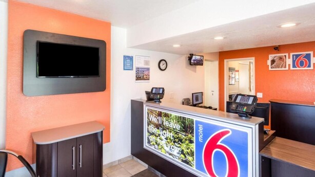 A motel reception desk with a large sign, a television mounted on the wall, and a clock.
