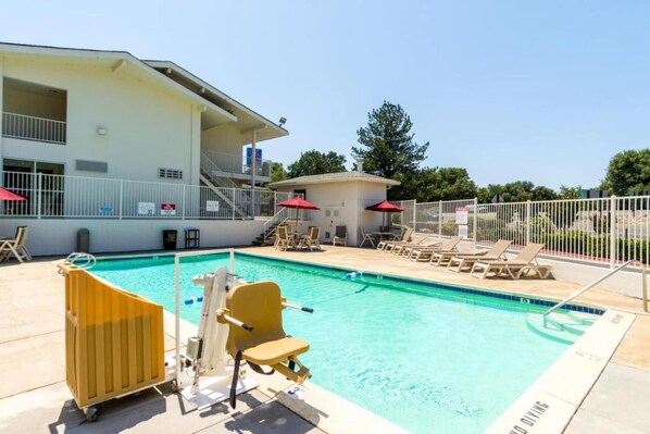 A swimming pool with lounge chairs and a lifeguard chair, a building with a balcony, and a fenced area.