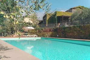 Une piscine à l’eau claire, entourée de verdure, et un bâtiment doté d’un balcon.
