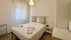 Ein Hotelzimmer mit Bett, Nachttisch, Lampe, Fenster mit Vorhängen und Spiegel.